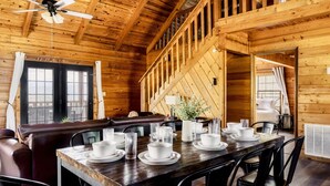 A wooden cabin with a dining area featuring a wooden table set for four, a leather booth, and a staircase leading to an upper level. - Stunning VIEWS, Luxury, Golf, Hot Tub, Arcade, Pet Friendly & Nearby Attractions (Sevierville)