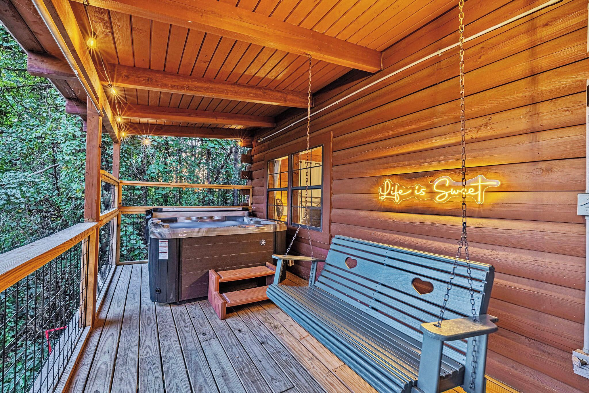 Una cabaña de madera con terraza de madera, un banco, un jacuzzi y un letrero de neón que dice "Lake is Sweet".