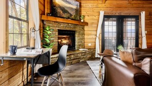A cozy cabin interior with a stone fireplace, wooden walls, a leather couch, and a dining area with a table and chairs. - Stunning VIEWS, Luxury, Golf, Hot Tub, Arcade, Pet Friendly & Nearby Attractions (Sevierville)