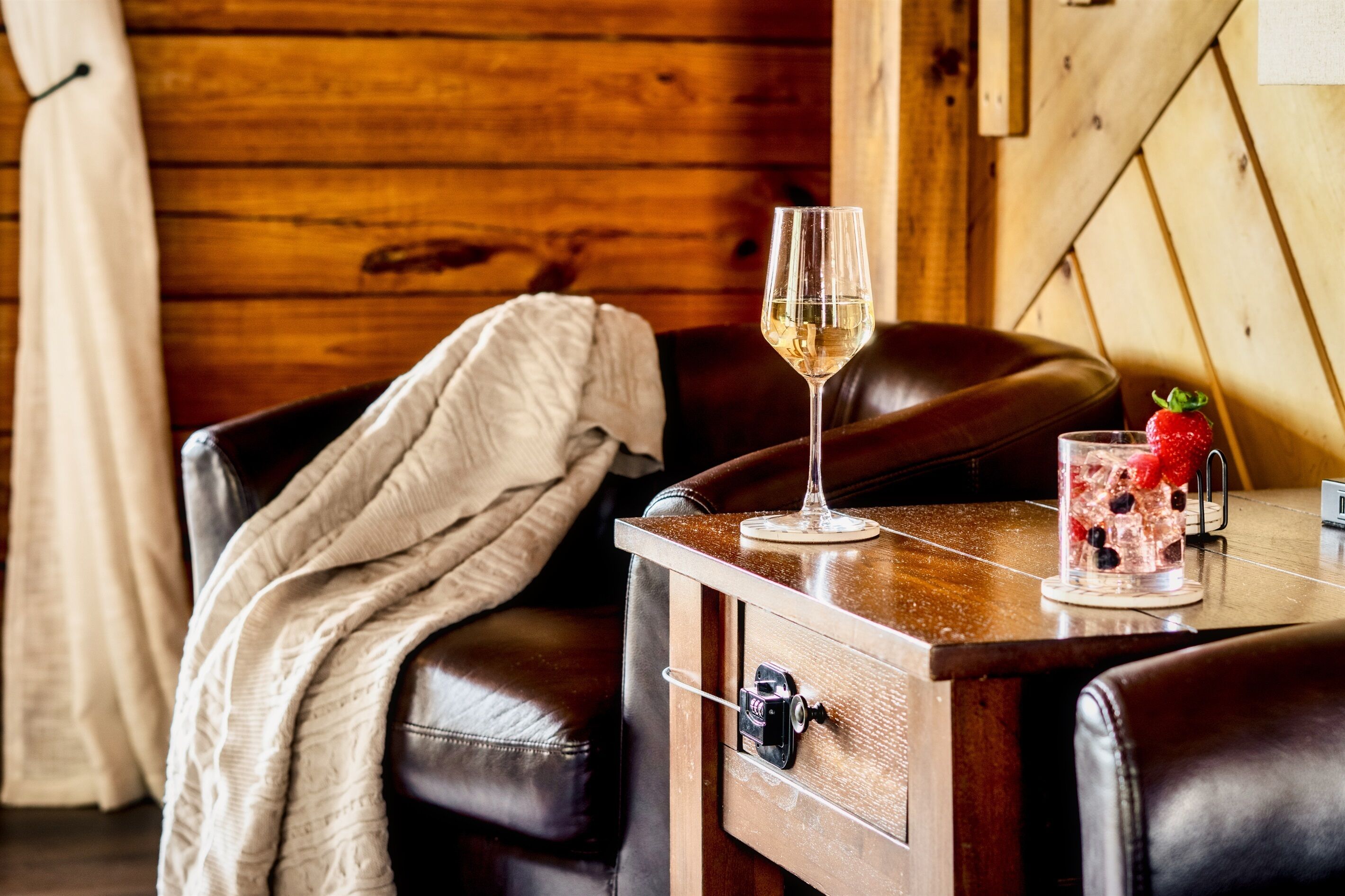 A wooden interior with a leather chair, a glass of white wine, and a fruit-infused drink on a wooden table.