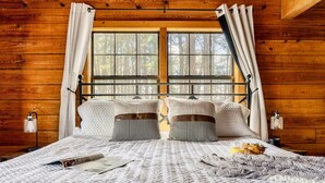 A wooden cabin bedroom with a large bed, two bedside lamps, and a window with curtains. - Stunning VIEWS, Luxury, Golf, Hot Tub, Arcade, Pet Friendly & Nearby Attractions (Sevierville)