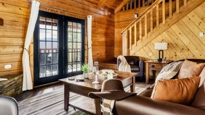 A cozy wooden cabin interior with a dining table, a sofa, and a staircase. - Stunning VIEWS, Luxury, Golf, Hot Tub, Arcade, Pet Friendly & Nearby Attractions (Sevierville)