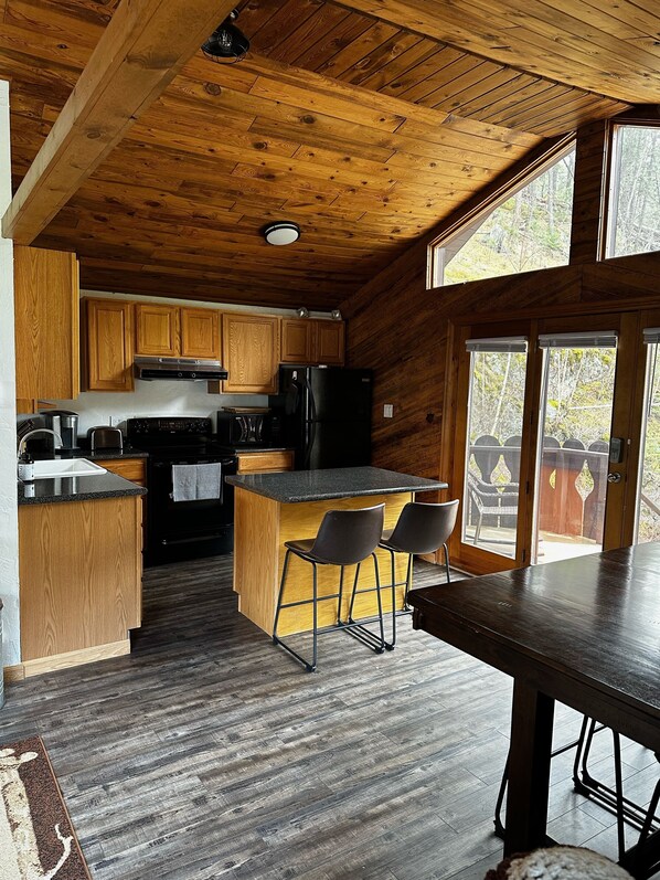 A wooden cabin kitchen with a central island, bar stools, and a dining table.