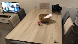 Ruokapöytä tuoleineen, televisio jalustalla, lautasliinalla varustettu kulho ja pöydällä oleva laatikko, jonka kyljessä lukee ”FORTWEST”.