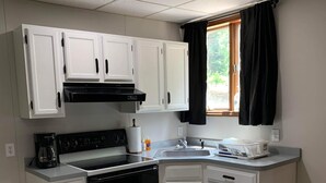 A compact kitchen with white cabinets, a black stove, and a window with black curtains. - Outlaw Lodge (Hatfield 1st Floor) ATV,SXS Offroad (Iaeger)