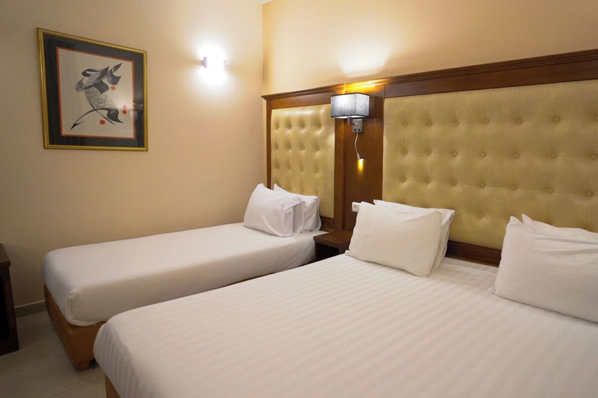 A hotel room with two single beds, a large mirror, and a wall-mounted light fixture.