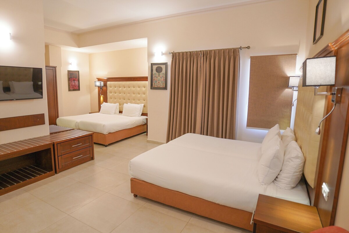 A hotel room with two beds, a TV, a desk, and a shower area.