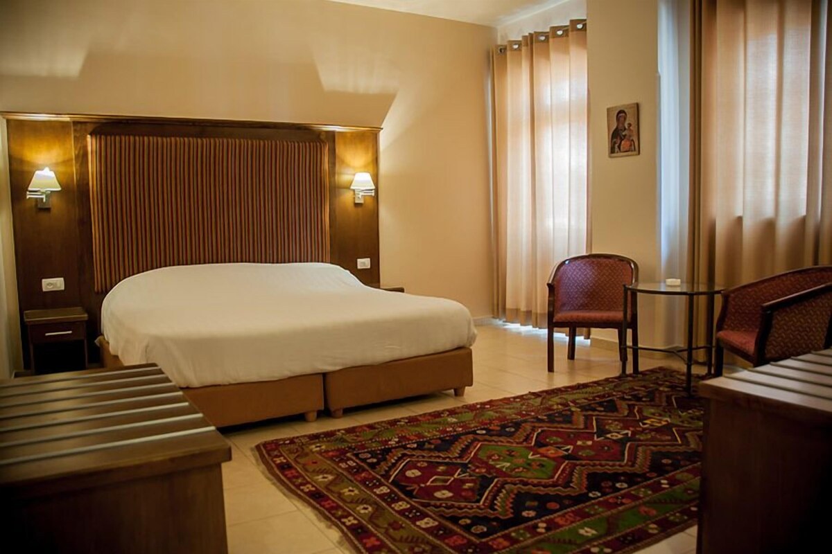 A hotel room with a large bed, a small table, a chair, and a decorative rug.
