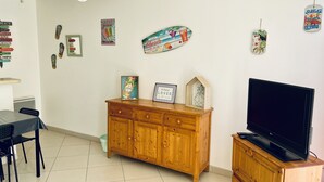 Een woonkamer met een houten kast, een televisie en verschillende wanddecoraties, waaronder een bord met een strandthema en een kunstwerk van een ananas.
