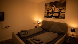 A bedroom with two beds, a painting on the wall, and bedside lamps.