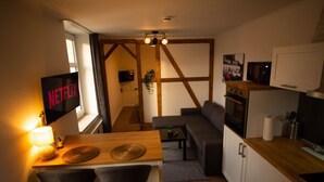 A compact living space with a kitchenette, a dining area with a table and chairs, a sofa, and a TV mounted on the wall.
