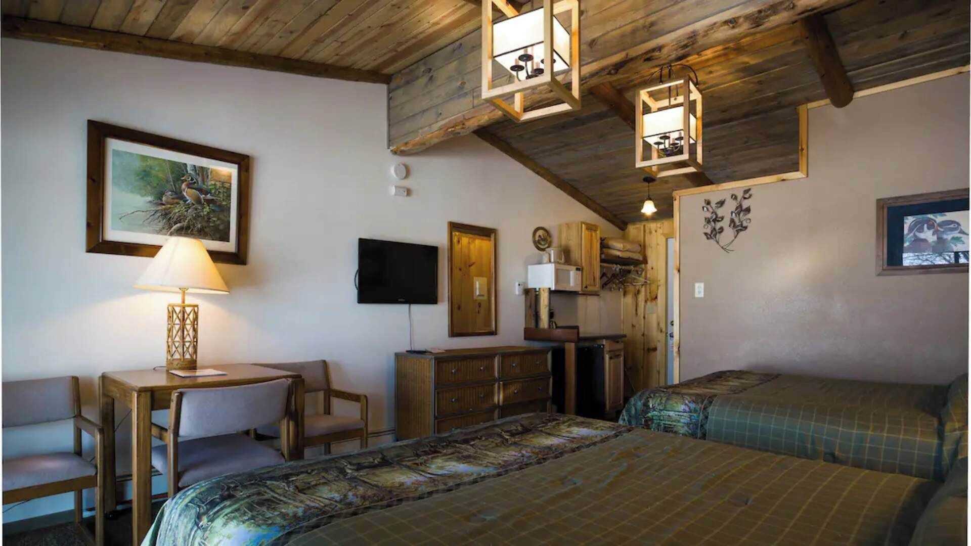 A cozy room with a bed, a desk with a lamp, a TV, and wooden walls.
