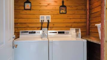 A laundry room with two white washers and dryers, wooden walls, and a ceiling light.