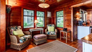 L’intérieur chaleureux d’un chalet avec des murs en bois, deux fauteuils en osier dotés de coussins, une petite table avec une lampe et un coin cuisine.