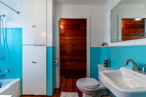 Ein Badezimmer mit Holztür, Toilette in Weiß, Waschbecken in Weiß und einer Badewanne.