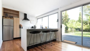 A modern kitchen with a stainless steel refrigerator, wooden cabinets, and a large window overlooking a garden.