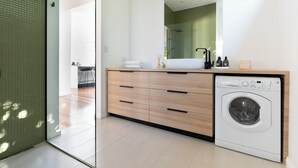 A modern bathroom with a built-in washing machine, a large mirror, and a wooden vanity with drawers.