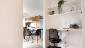 A modern kitchen with wooden cabinets, a dining table with chairs, and a black office chair in a bright room with white walls and wooden flooring. - Walter Cottage: As Cosy as it is Convenient (South Launceston)