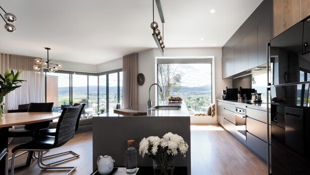 A modern kitchen with stainless steel appliances, a dining area with a view, and a large window overlooking a cityscape. - Impressively Spacious, Modern & Convenient (Newstead)