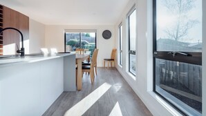 A modern kitchen with a central island, wooden chairs, and large windows offering a view of the backyard. - Modern & Convenient in Newstead (Newstead)