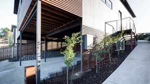A modern building with a covered outdoor area, steps leading to a wooden deck, and young trees planted in the ground. - Modern & Convenient in Newstead (Newstead)