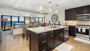 A modern kitchen with dark cabinets, stainless steel appliances, and pendant lighting. - Hawaii Life Rentals Presents Puu Poa 302 (Princeville)