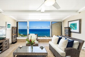 Una sala de estar con vista al océano, muebles de mimbre y un televisor.