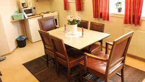 A dining area with a table set for four, surrounded by wooden chairs. A small kitchen with a microwave and stove is visible in the background. - Peaceful holiday apartment on a small farm, Tørberget in Trysil (Innlandet)