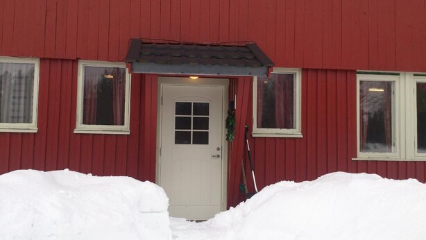 A red building with a white door, two windows with curtains, and a snow-covered entrance. - Peaceful holiday apartment on a small farm, Tørberget in Trysil (Innlandet)