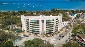 Un hotel de varios pisos con un patio central, rodeado por una zona costera con barcos en el agua.