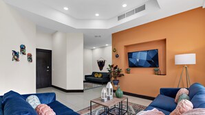 Un salón moderno con sofás azules, una mesa de centro y una pared grande de color naranja.