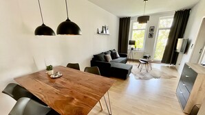 Un salon moderne avec une table à manger en bois, des canapés noirs et des luminaires suspendus.