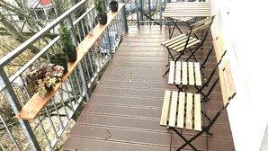 Une terrasse en bois avec des rampes en métal, des plantes en pot et des chaises pliantes en bois.