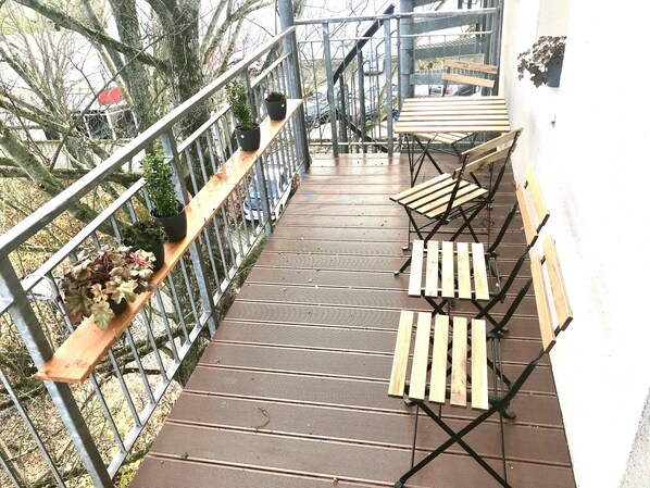 A wooden deck with metal railings, potted plants, and foldable wooden chairs.