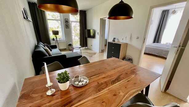 Un salon moderne avec une table à manger en bois, des chaises noires et des luminaires suspendus.