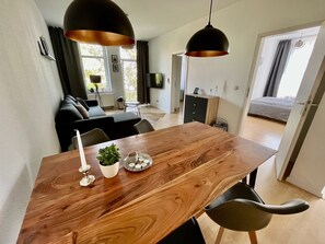A modern living room with a wooden dining table, black chairs, and pendant lights.