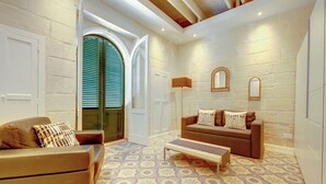 Ein Zimmer mit einem gemusterten Boden, einem braunen Sofa, einer Bank und einer Tür mit grünen Fensterläden.