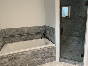 Bathroom features a bathtub, glass shower enclosure, and stone tile backsplash.