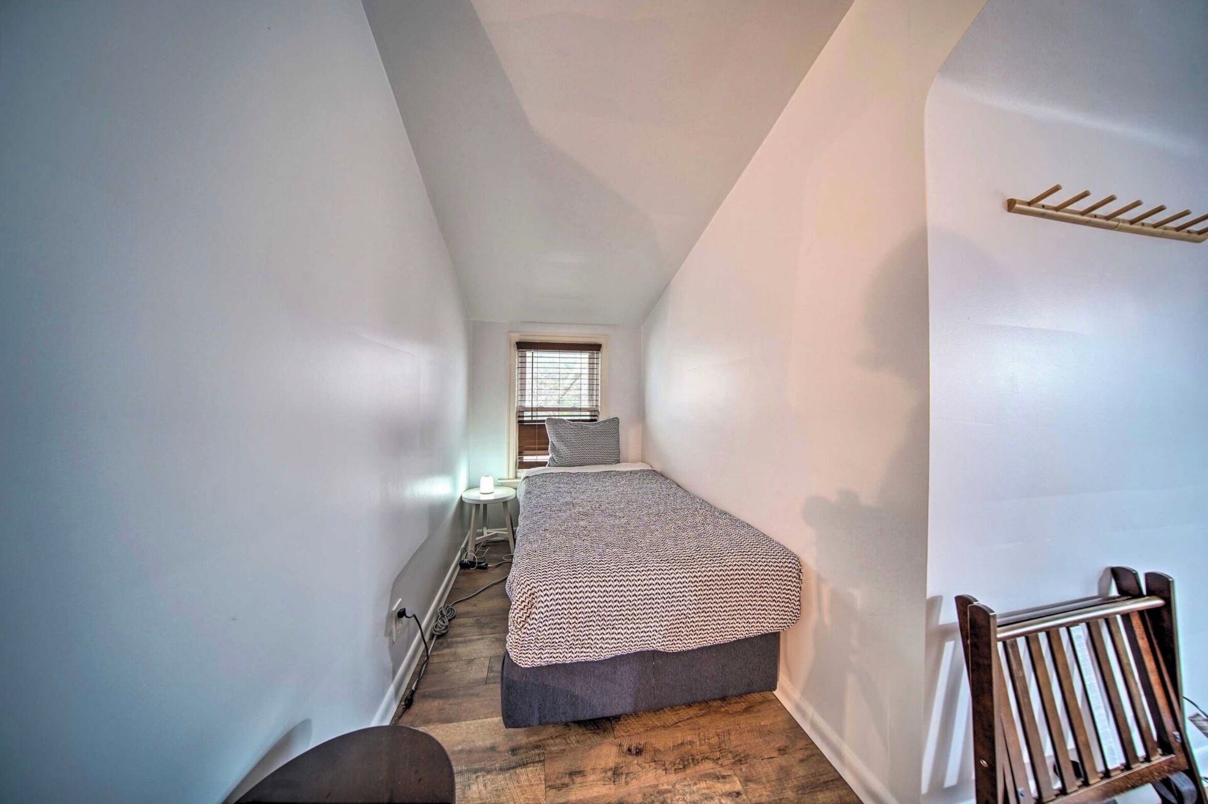 A narrow attic bedroom with a bed, a small desk, and a window.