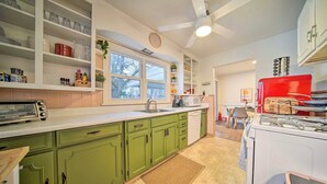Une cuisine avec des meubles de couleur verte, un plan de travail blanc, une cuisinière rouge et une fenêtre donnant sur des arbres.