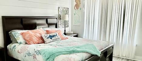 A bedroom with a bed, a ceiling fan, a nightstand, a lamp, and a window with curtains.