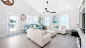 A spacious living room with a large sectional sofa, a blue sofa, and a white sofa. There is a ceiling fan, a clock, and a painting on the wall. - 3min walk to beach,hot tub, b-ball, pet friendly, parking for RV’s (Bolivar Peninsula)