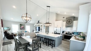 A modern kitchen with a central island, bar stools, and a dining area with a table and chairs. - 3min walk to beach,hot tub, b-ball, pet friendly, parking for RV’s (Bolivar Peninsula)