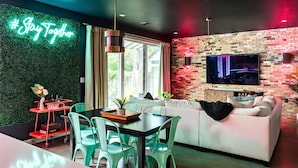 Ein modernes Wohnzimmer mit grüner Wand, einem weißen Sofa und einer Essecke mit türkisfarbenen Stühlen.