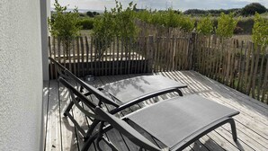 Un balcon avec deux chaises en métal, une clôture en bois et une vue sur un jardin et un paysage lointain.