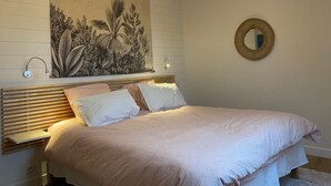 Une chambre à coucher comprenant un lit, une œuvre d’art accrochée au mur, un miroir rond et un luminaire fixé au plafond.
