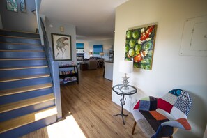 A spacious living area with a wooden staircase, a colorful sofa, and a dining area in the background.