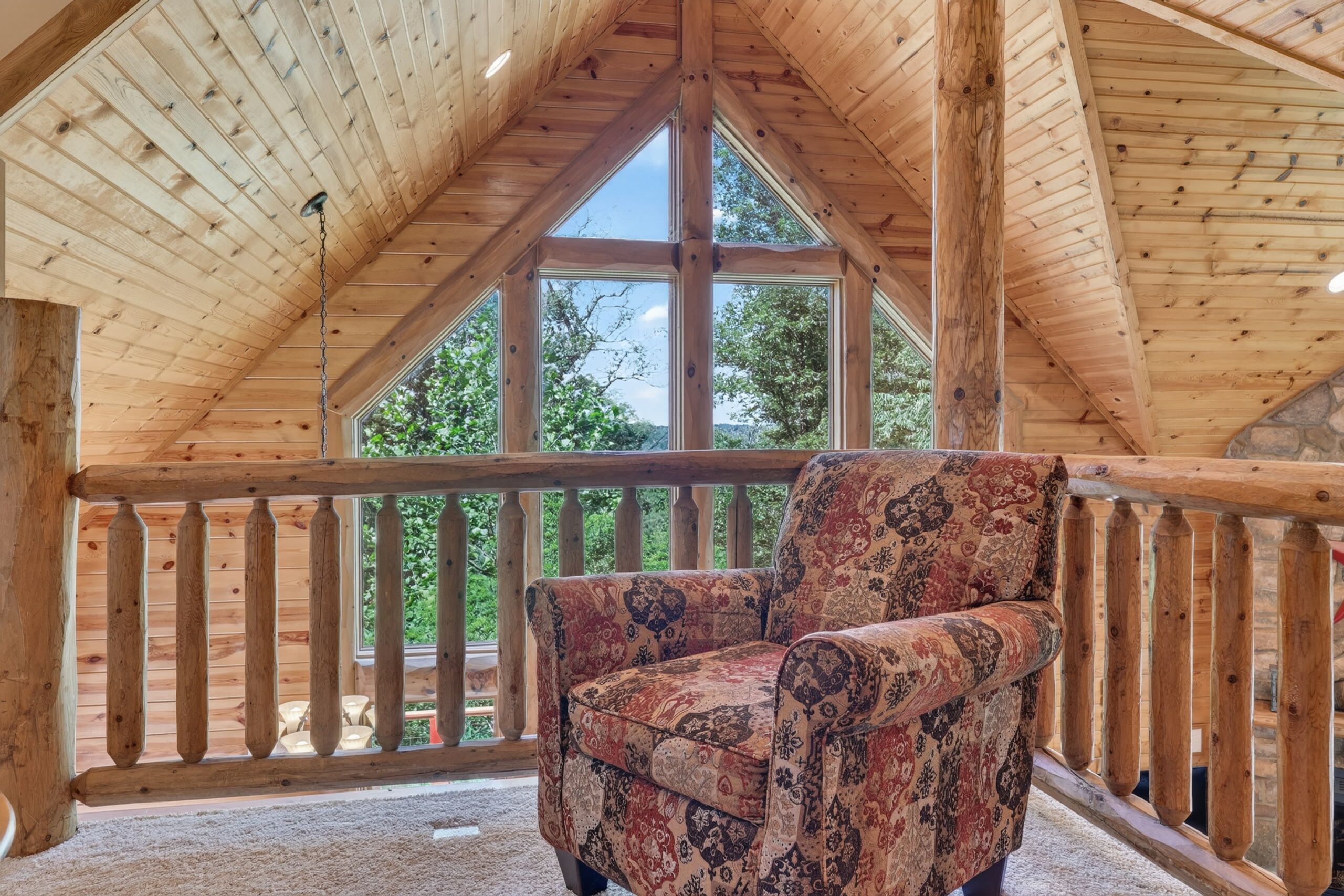 Un balcone in legno con vista sugli alberi, una poltrona con rivestimento decorativo e un soffitto in legno alto.