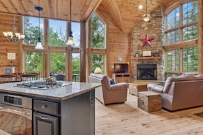 Ein Ferienhaus-Innenraum mit Kamin aus Stein, Holzwänden, einer Kücheninsel und einer gemütlichen Sitzecke.