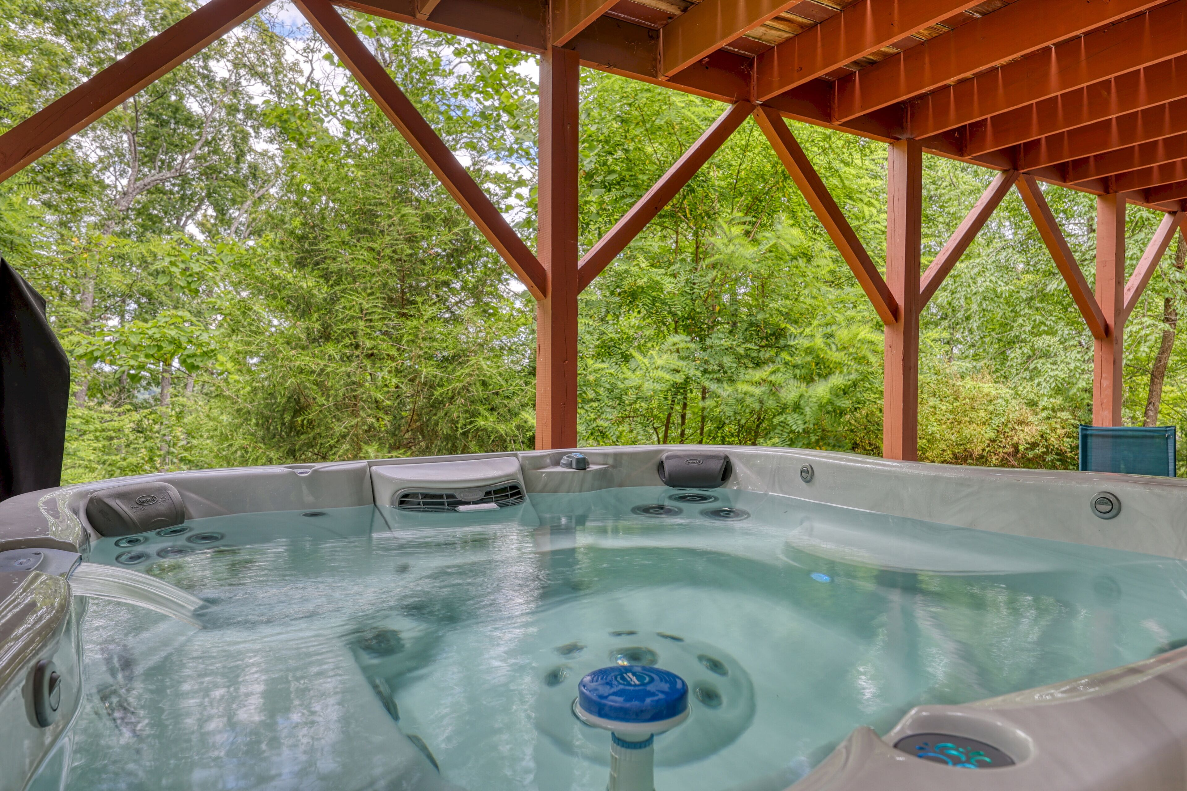 A hot tub under a wooden pavilion with a forest backdrop.